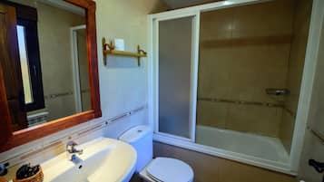 Un baño con lavamanos blanco, inodoro y ducha a ras de suelo con puerta de vidrio.