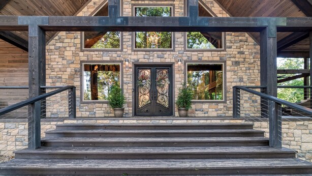 Un edificio de piedra con una escalera de madera que conduce a una puerta negra con paneles de vidrio decorativos.