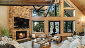 Amplia sala de estar con chimenea de piedra, asientos confortables y grandes ventanales con vistas al exterior.