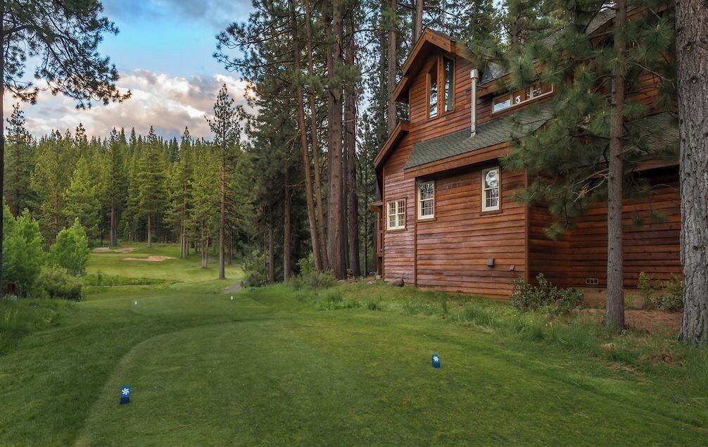 A wooden cabin with a porch, surrounded by a forest and a golf course.