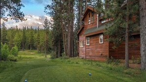 Une cabane en bois dotée d’un porche, entourée d’une forêt et d’un terrain de golf.