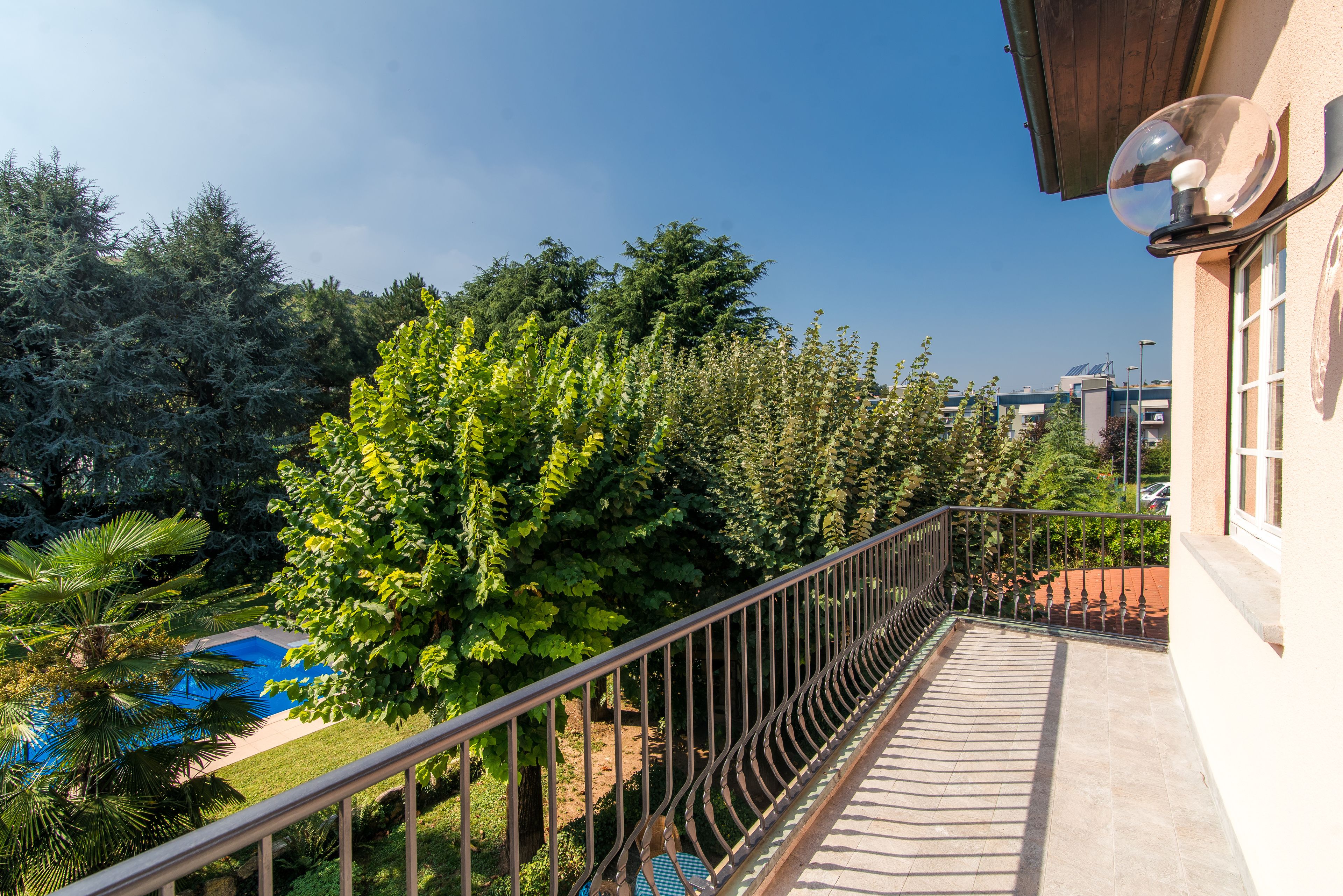 A balcony with a metal railing overlooking a swimming pool and lush greenery.