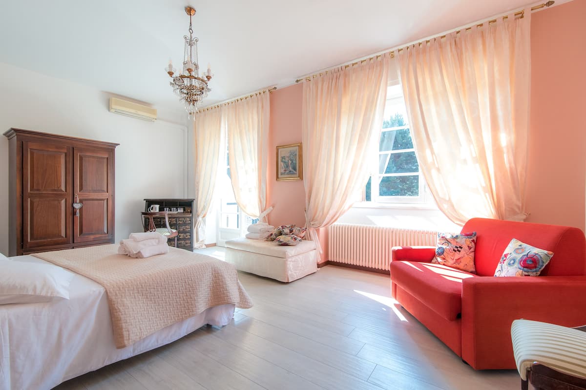 A bedroom with a bed, a red sofa, a wooden cabinet, and a window with curtains.