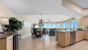 Una cocina moderna con una isla central, comedor con sillas y amplios ventanales con vistas.