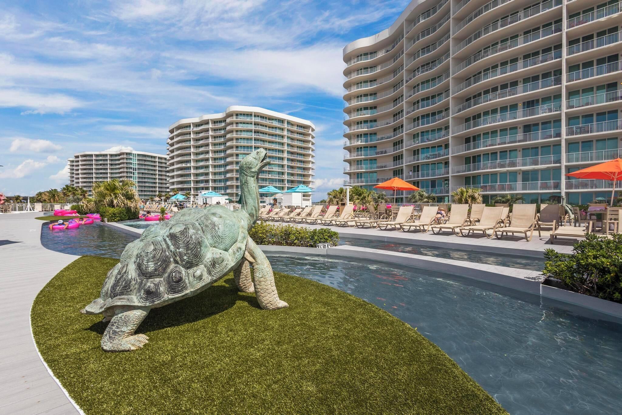 A swimming pool area with a large turtle sculpture, lounge chairs, and high-rise hotel buildings in the background.