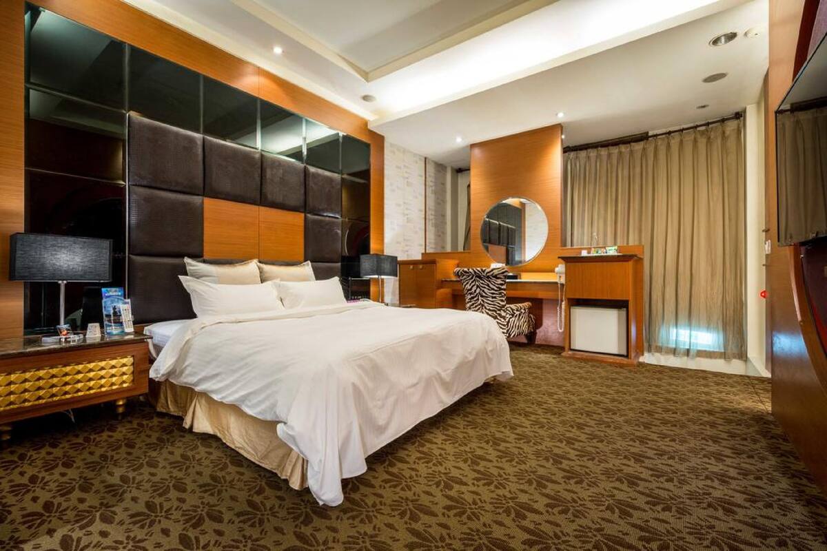 A hotel room with a large bed, a desk with a mirror, and a wardrobe.