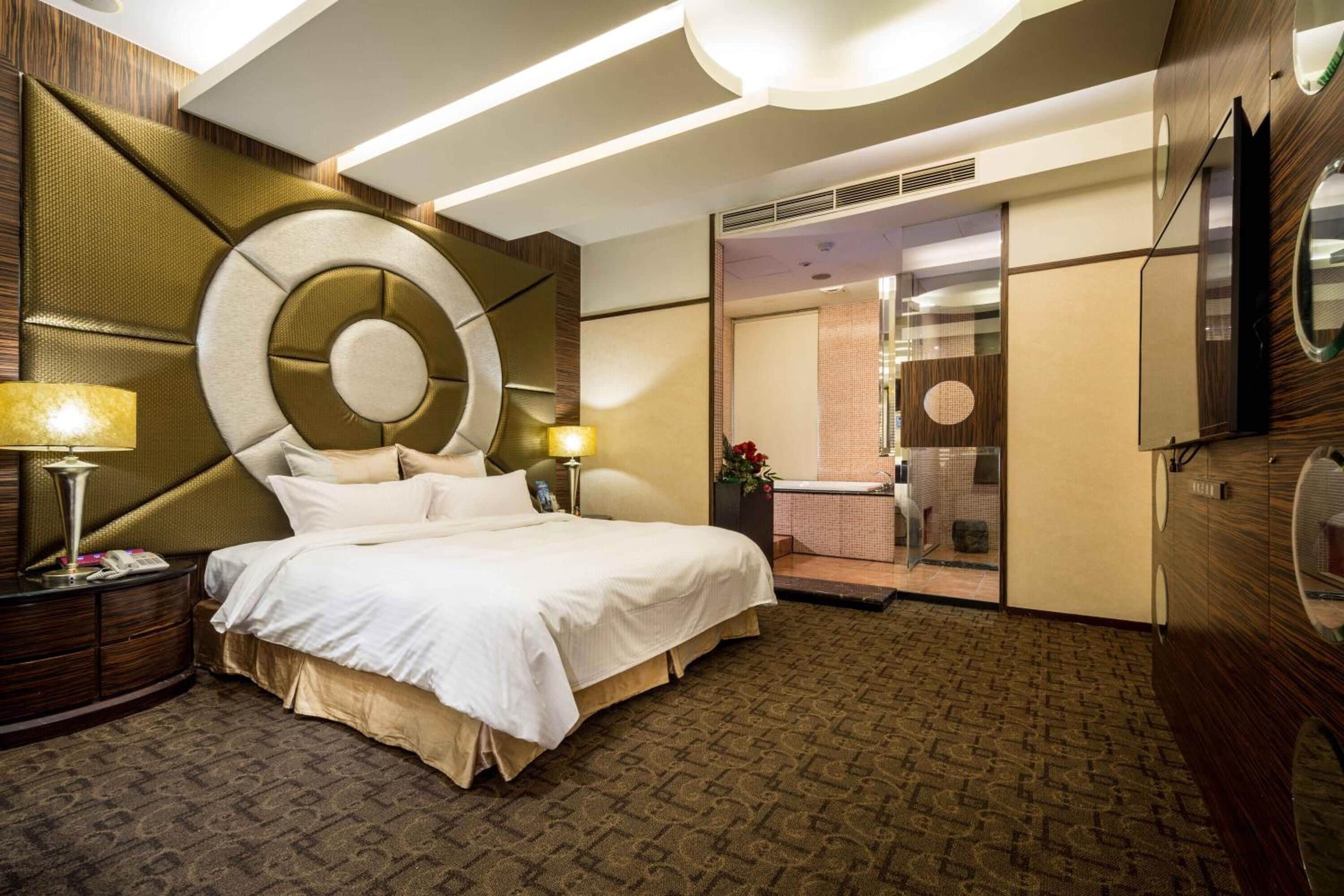 A hotel room with a large bed, a bedside table with a lamp, a mirror, and a view of a bathroom with a bathtub.