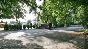 A parking area with a van and a car, surrounded by trees and a building with a tower. - Hotel Stockumer Hof (Werne)