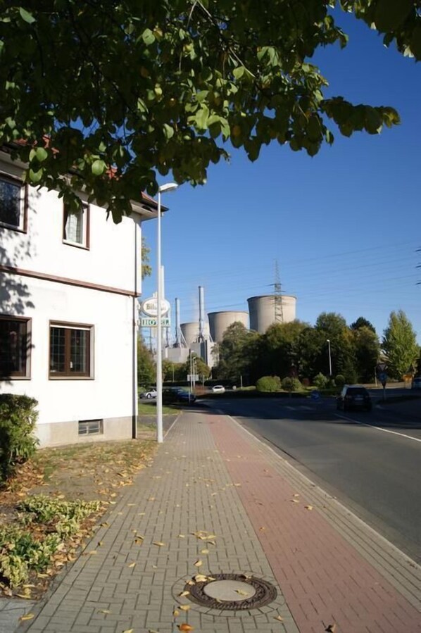 Una acera pavimentada con un edificio y estructuras industriales al fondo.