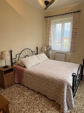 A bedroom with a bed, a nightstand, a lamp, a window with curtains, and a radiator. - Bed and Breakfast Elisa (Sonnino)