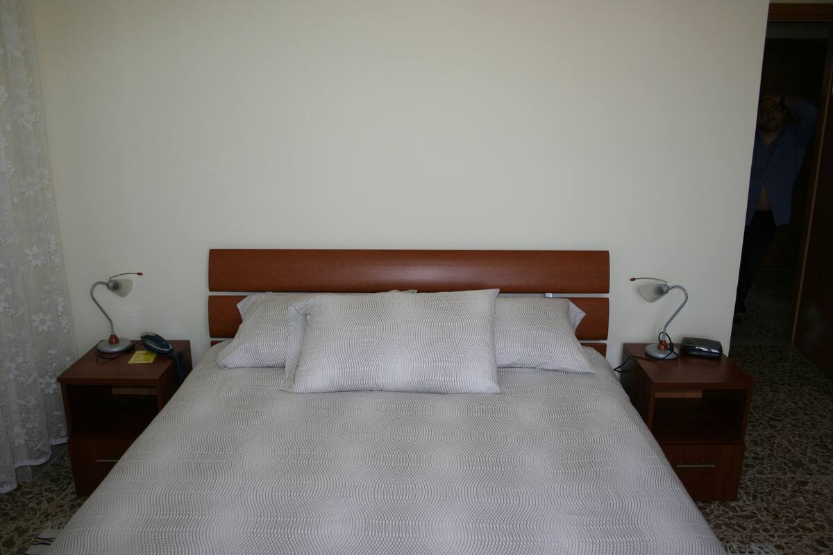 A neatly made bed with a wooden headboard, two bedside tables with lamps, and a patterned bedspread.