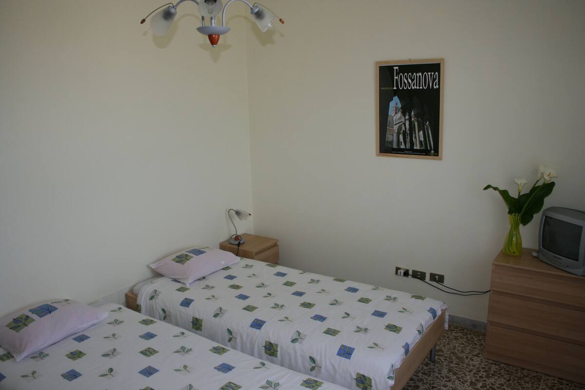 A bedroom with two beds, a nightstand, a dresser, a television, and a poster on the wall.