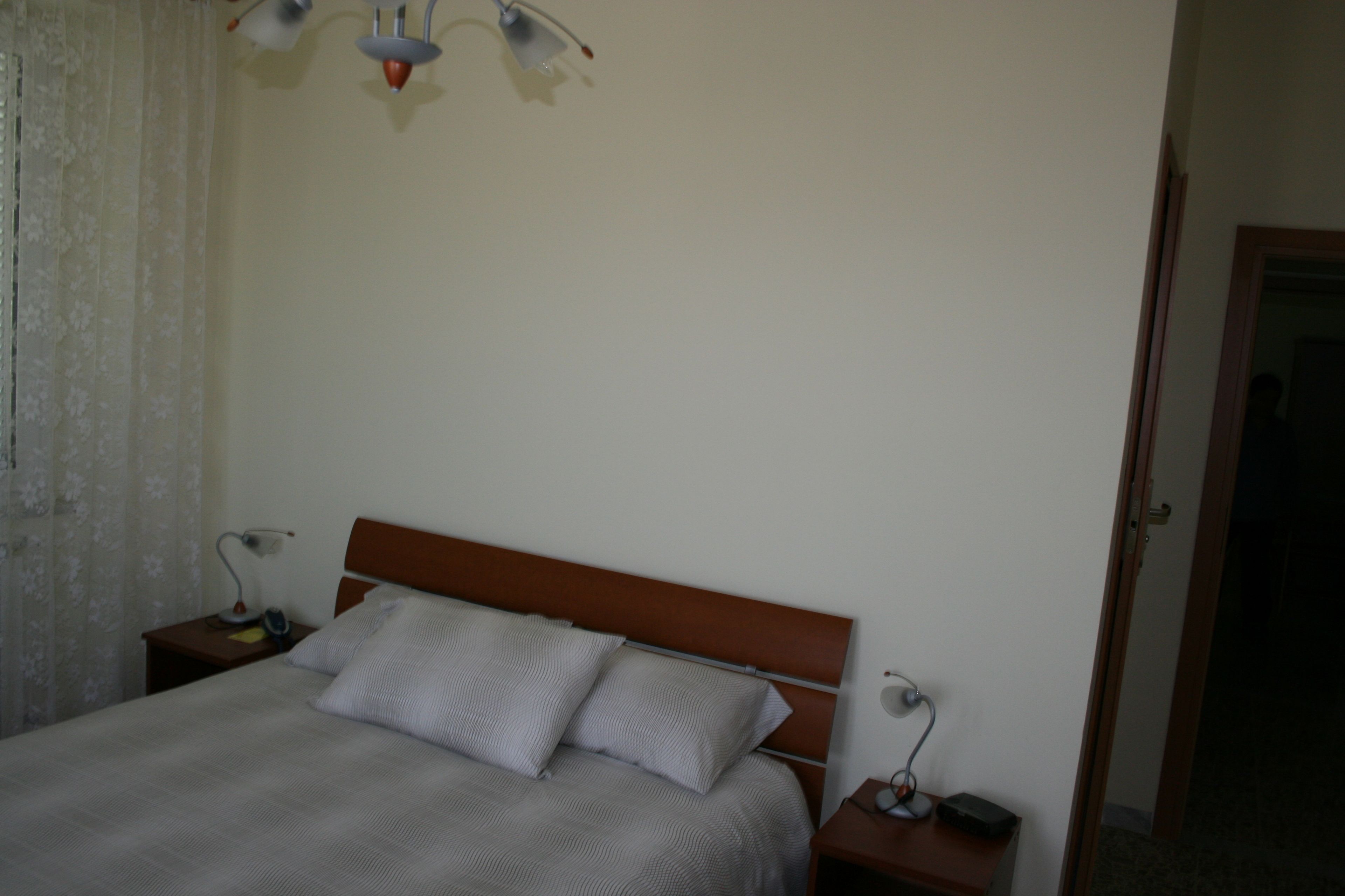 Un dormitorio con una cama, dos mesitas de noche, una lámpara y una puerta.
