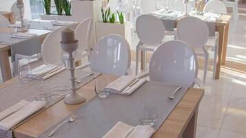 A modern dining area with white chairs and tables, large windows, and indoor plants.