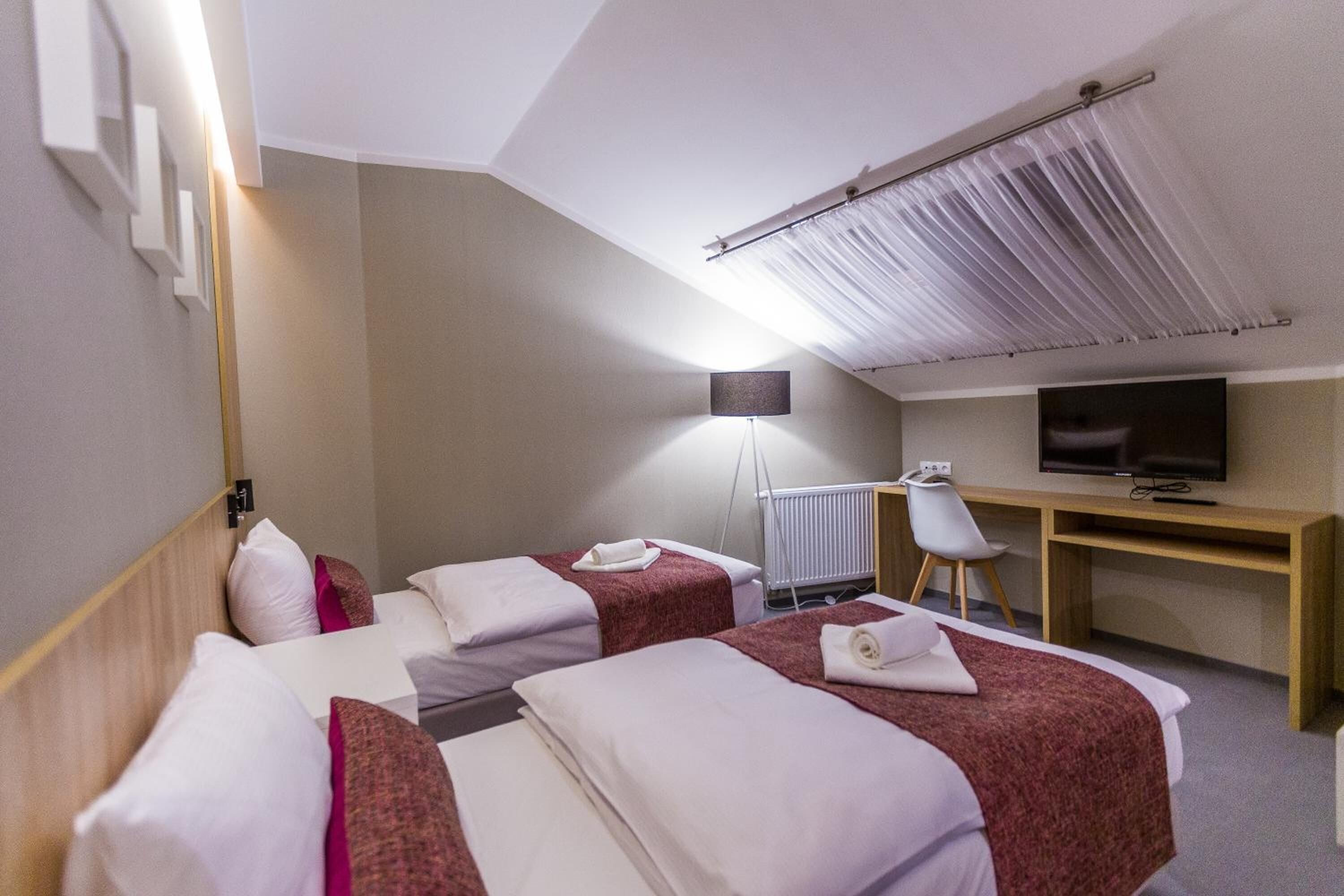 Une chambre d’hôtel avec deux lits, un bureau, une chaise, un téléviseur et un radiateur.