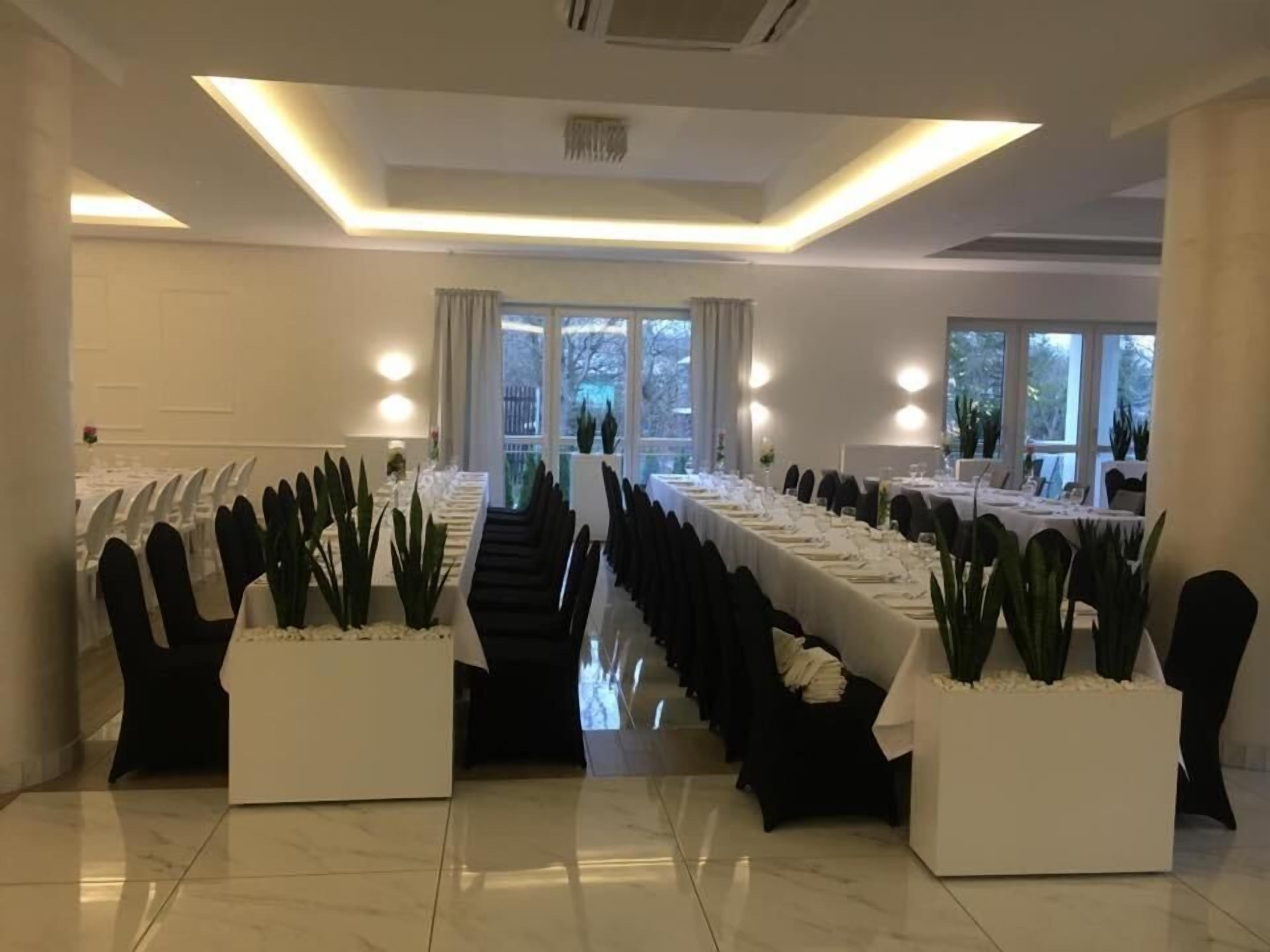 Un salón de conferencias con mesas largas, sillas negras y plantas en macetas.