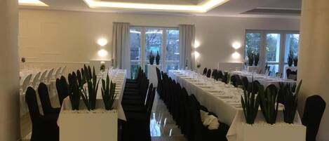 A conference room with long tables, black chairs, and potted plants.