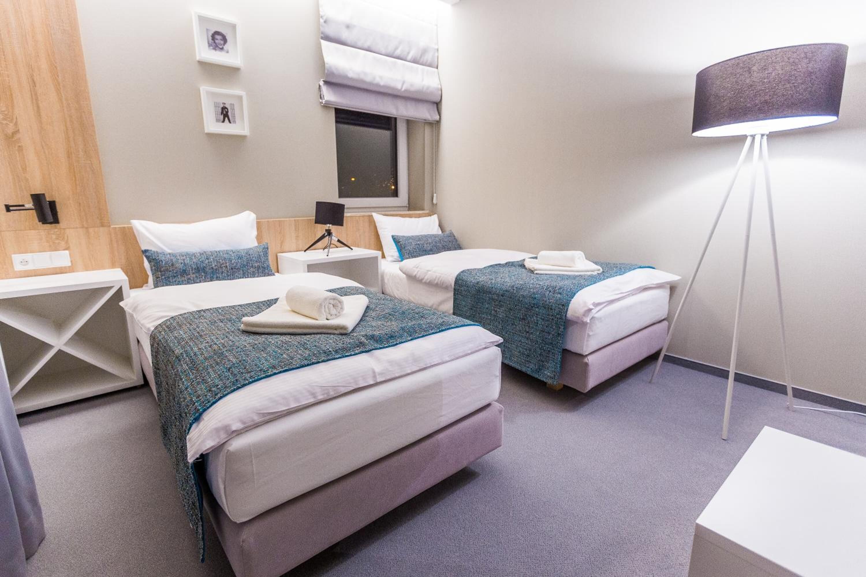 Une chambre d’hôtel avec deux lits, une table de chevet avec une lampe et une fenêtre avec des stores.