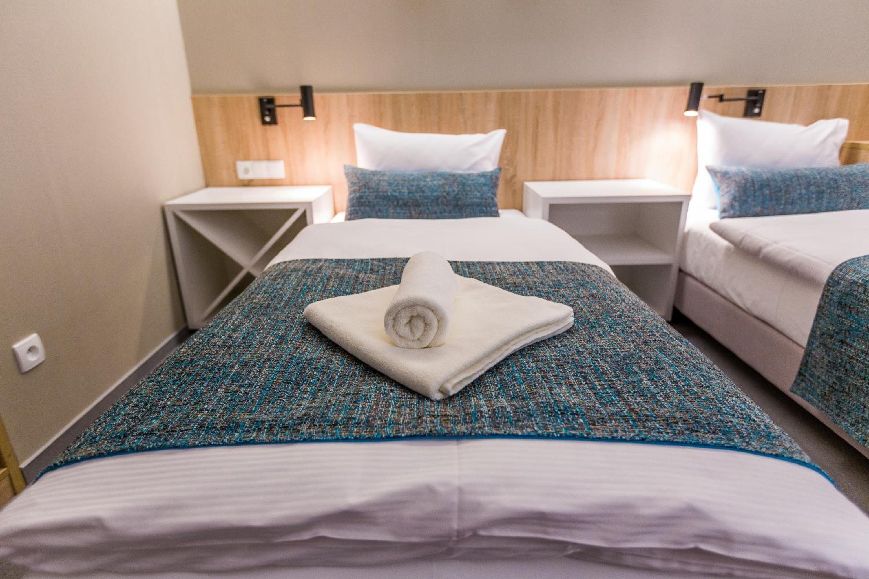 A hotel room with two beds, each with a blue and white patterned bedspread, a white towel on the headboard, and a wooden headboard.