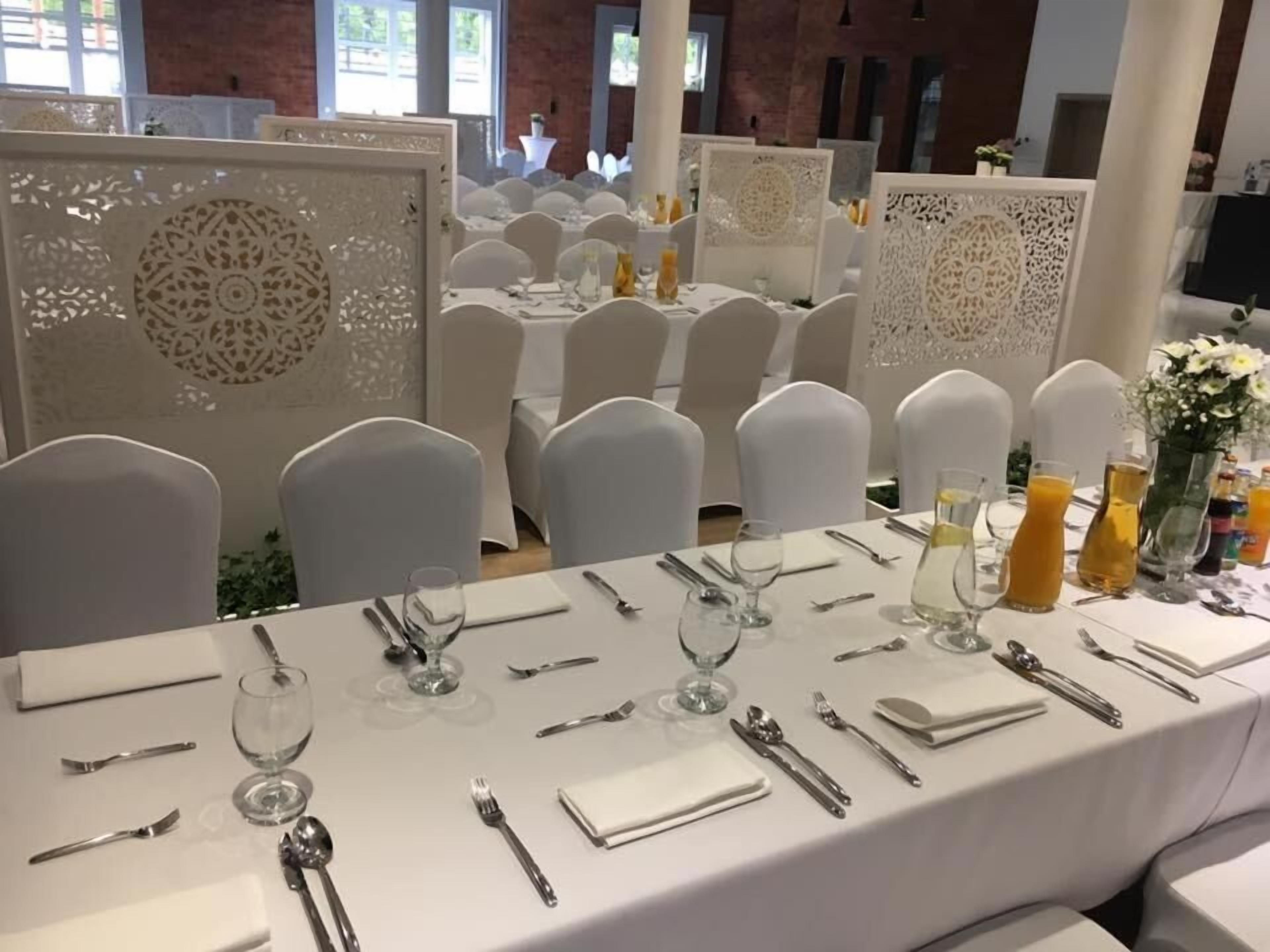Ein Festsaal mit runden Tischen, gedeckt für eine festliche Veranstaltung, mit weißen Tischdecken, Gläsern und Besteck.