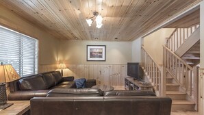 A cozy living room with a wooden ceiling, a large leather sofa, a television, and a staircase. - Clean and fresh remodeled Lake Forest Glen End Unit (Tahoe City)
