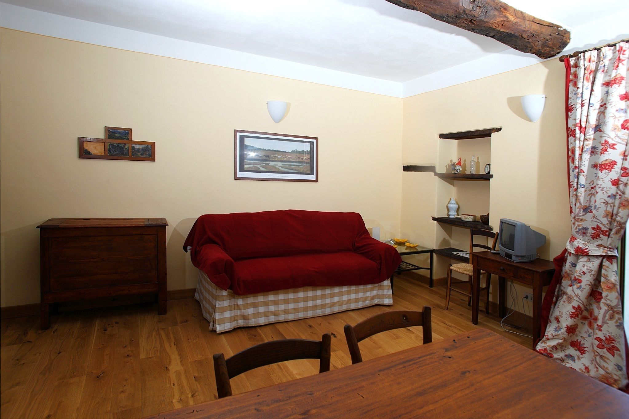 Une pièce chaleureuse avec une table en bois, un canapé rouge, une commode en bois, un téléviseur et un tableau encadré accroché au mur.