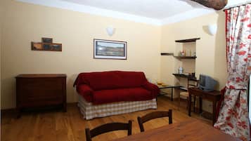 Une pièce chaleureuse avec une table en bois, un canapé rouge, une commode en bois, un téléviseur et un tableau encadré accroché au mur.