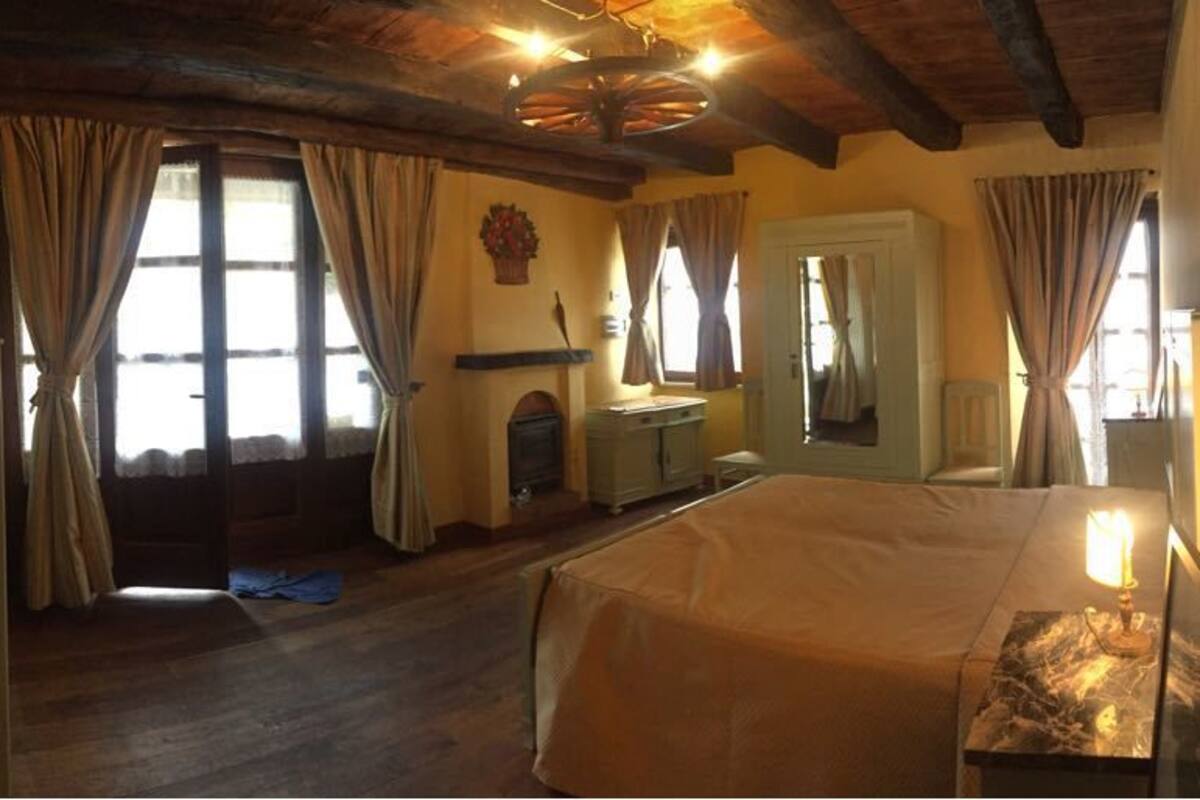 Un dormitorio con una cama grande, suelo de madera, una chimenea y un espejo.