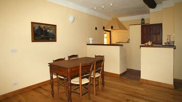 Uma área de refeições com mesa e cadeiras de madeira, um quadro na parede e uma cozinha com armários e bancada.