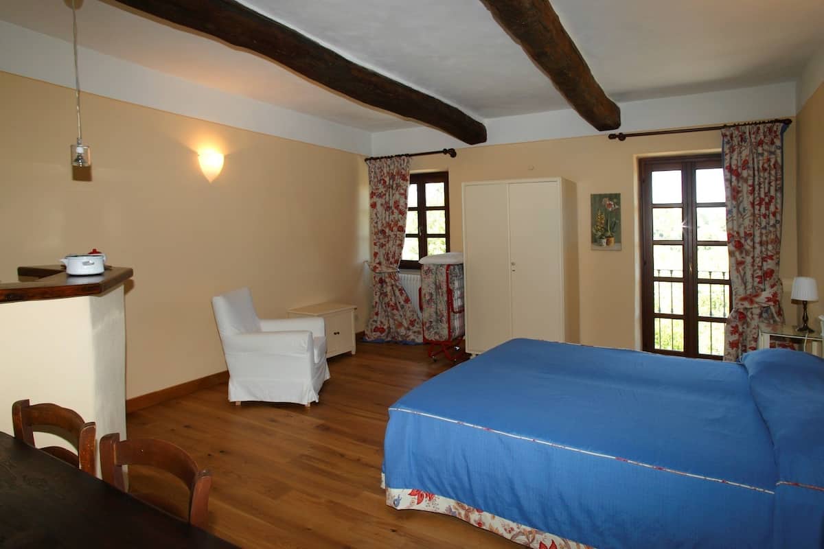 Un dormitorio con cama, una silla, un escritorio y ventana con cortinas.