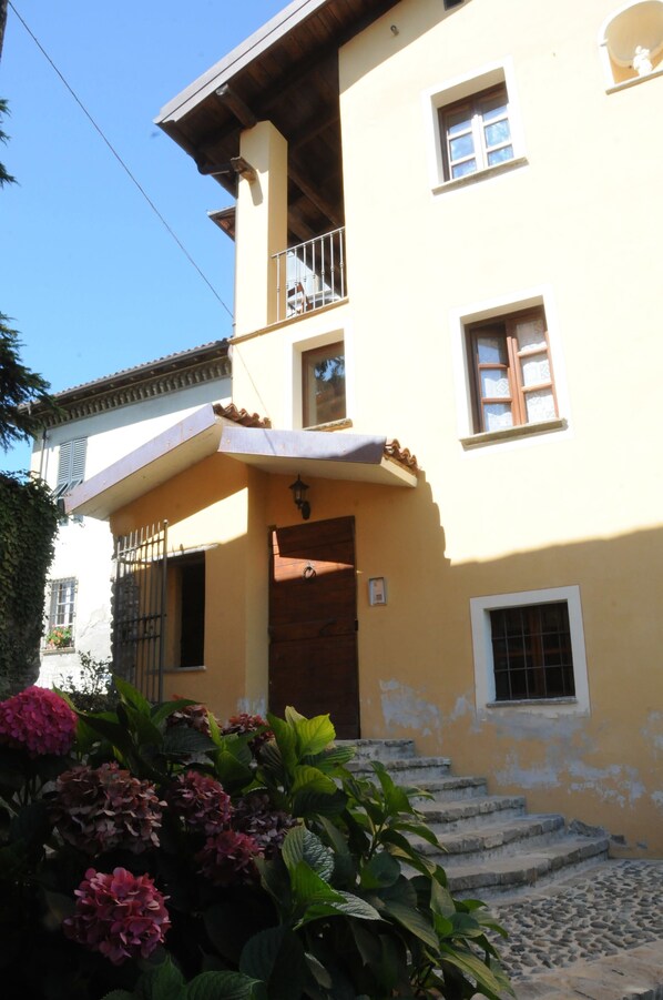 A two-story building with a balcony on the upper floor, a wooden door, and steps leading to the entrance.