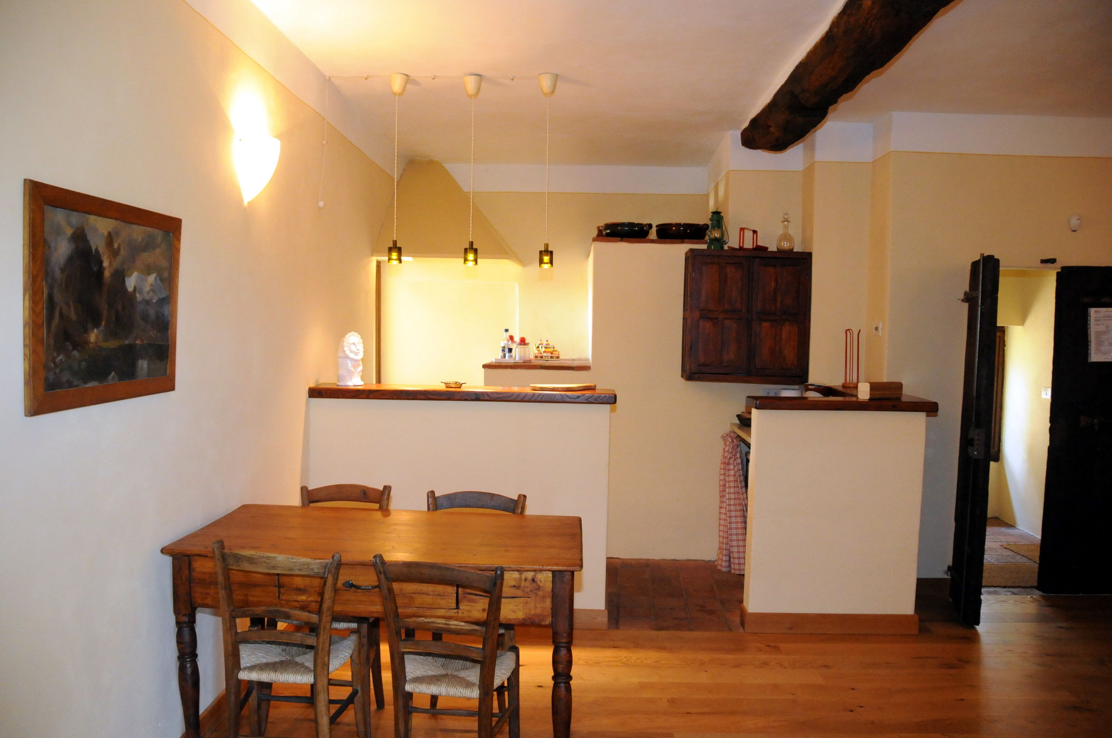 Un comedor con mesa y sillas de madera, una cocina con mostrador y armarios, y un pasillo que lleva a una puerta.