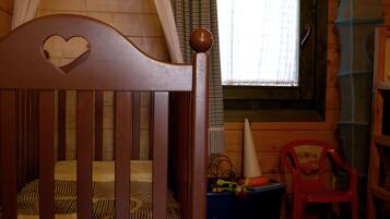 Una cuna de madera con un corte en forma de corazón, una ventana con cortinas y una silla roja de plástico.
