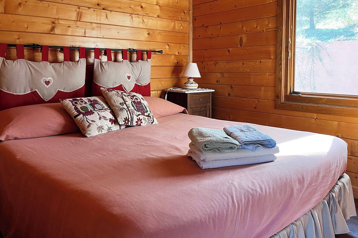 Un lit bien fait, avec une literie rose, deux coussins décoratifs et des serviettes pliées posées sur le lit.