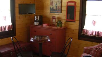 A cozy room with a wooden interior, a small round table with chairs, a red dresser, a television mounted on the wall, and a vintage telephone.