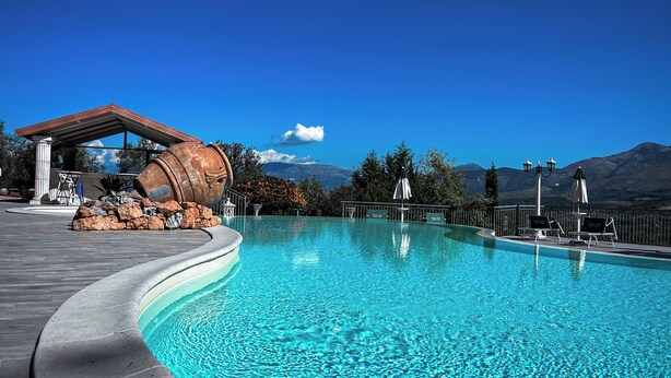 A swimming pool with a curved edge, a large barrel sculpture, and a view of mountains in the background.