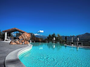 Une piscine à bord incurvé, une grande sculpture en forme de tonneau et une vue sur les montagnes en arrière-plan.