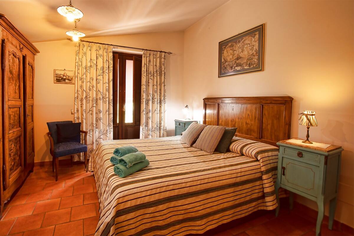 Une chambre à coucher comprenant un lit, une chaise, une table de chevet et une porte donnant sur une autre pièce.