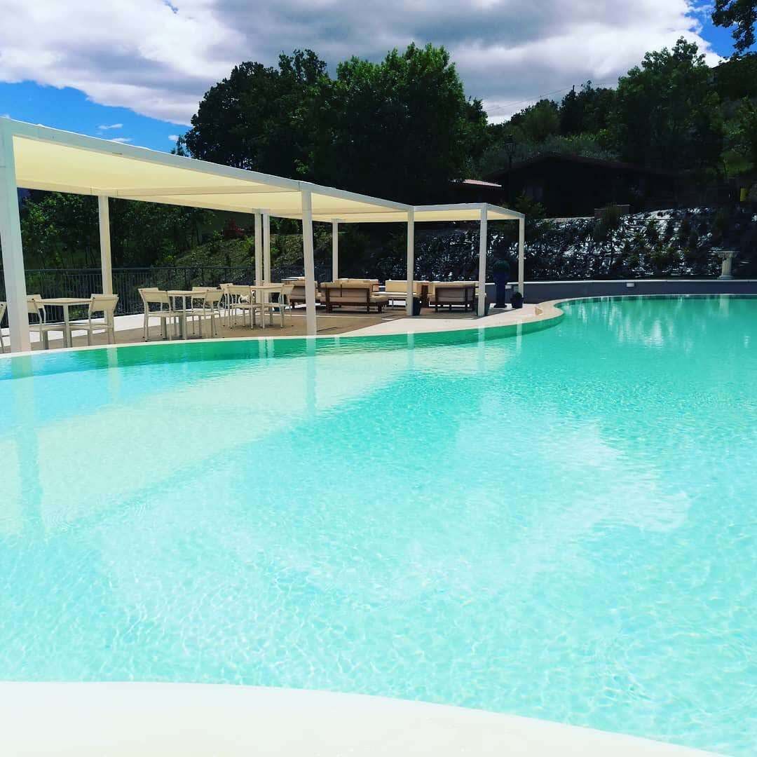 Una piscina azul cristalina con una zona de estar techada y sillones de descanso.