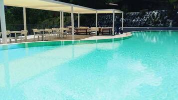 Una piscina azul cristalina con una zona de estar techada y sillones de descanso.