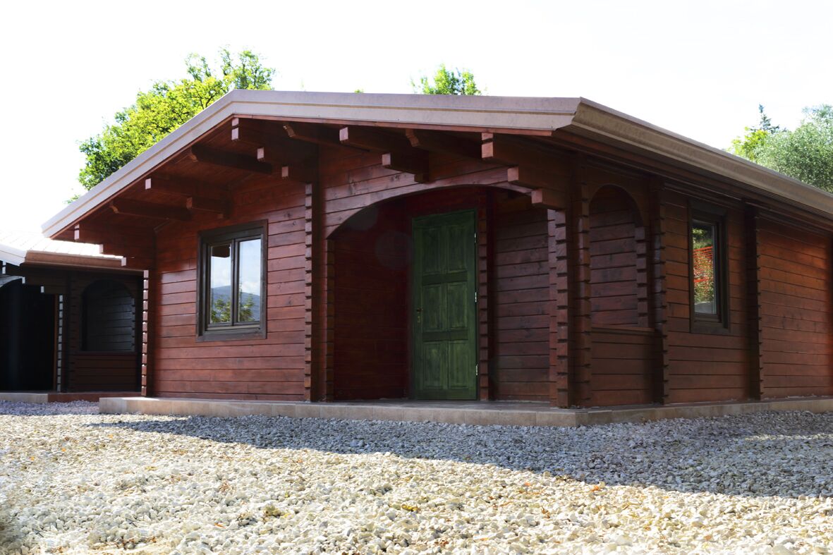 Une cabane en bois avec une porte verte, un porche couvert et une allée gravillonnée.