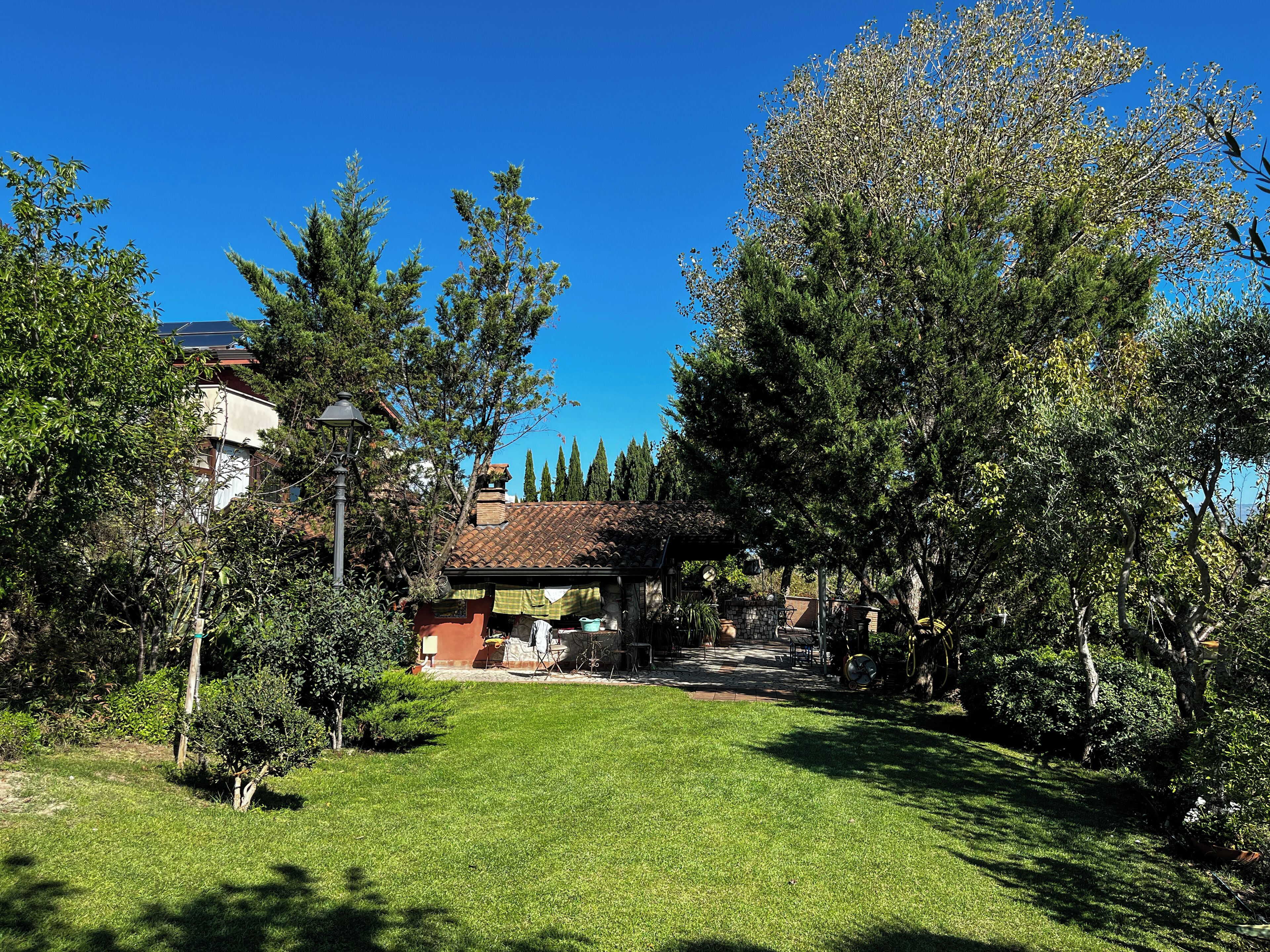 Un jardín bien cuidado con un patio, rodeado de árboles y un cielo azul despejado.