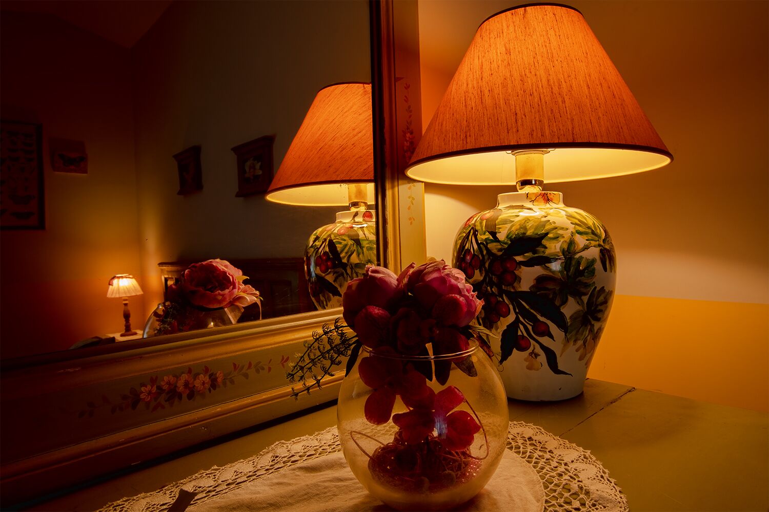 Una habitación con un espejo que refleja una lámpara y un florero con flores.