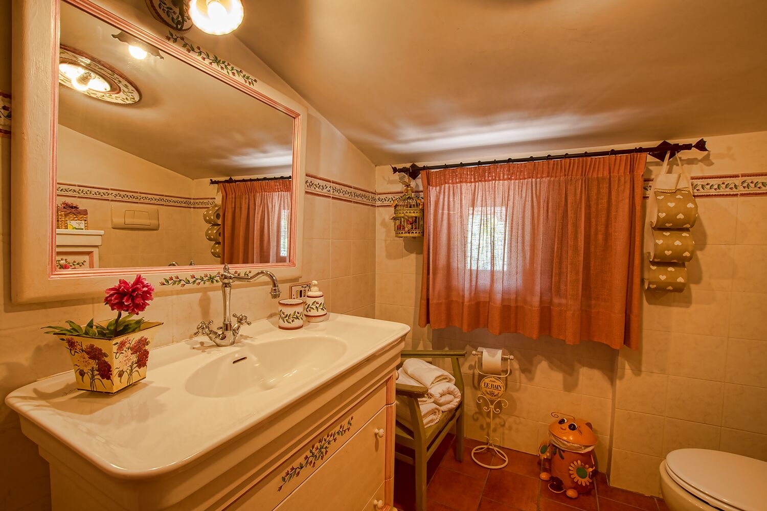 Un baño con lavamanos, espejo, tocador, inodoro y adornos.