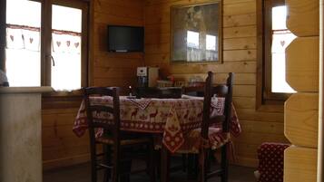 A wooden cabin with a dining table set for four, a television mounted on the wall, and a painting above the table.