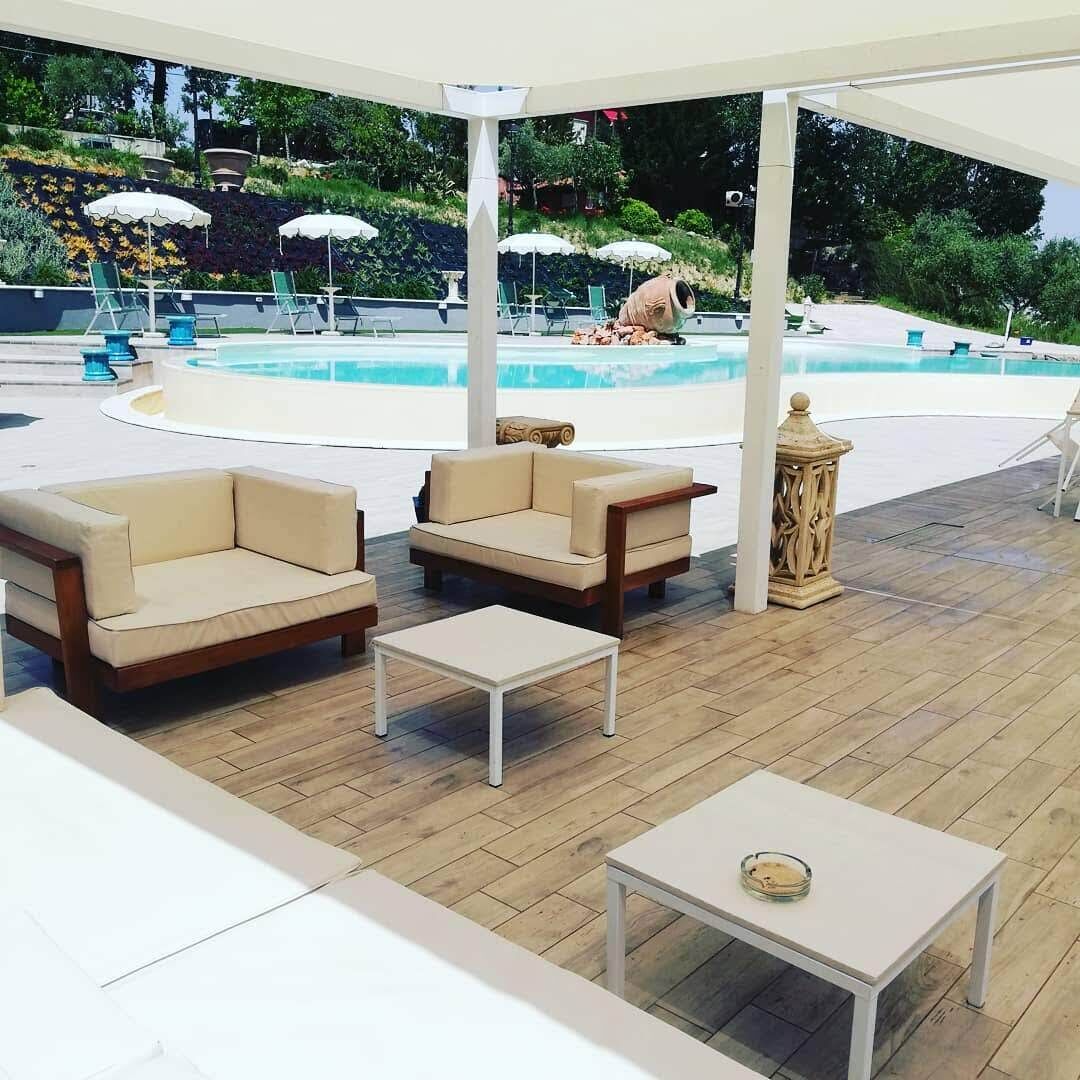 A covered outdoor seating area with two sofas and a small table, overlooking a swimming pool.