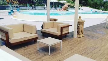 A covered outdoor seating area with two sofas and a small table, overlooking a swimming pool.