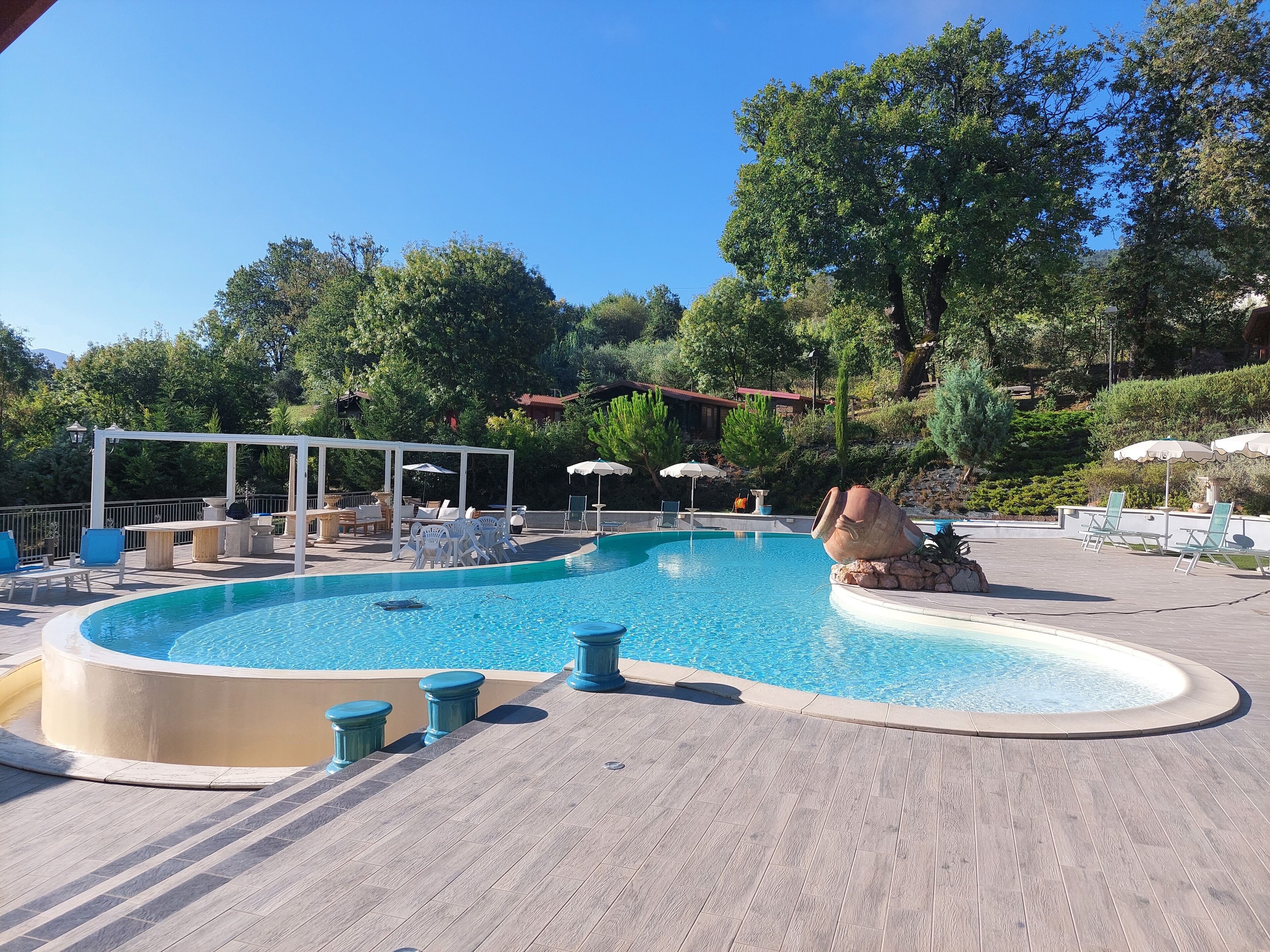 A swimming pool with a wooden deck, lounge chairs, and umbrellas.
