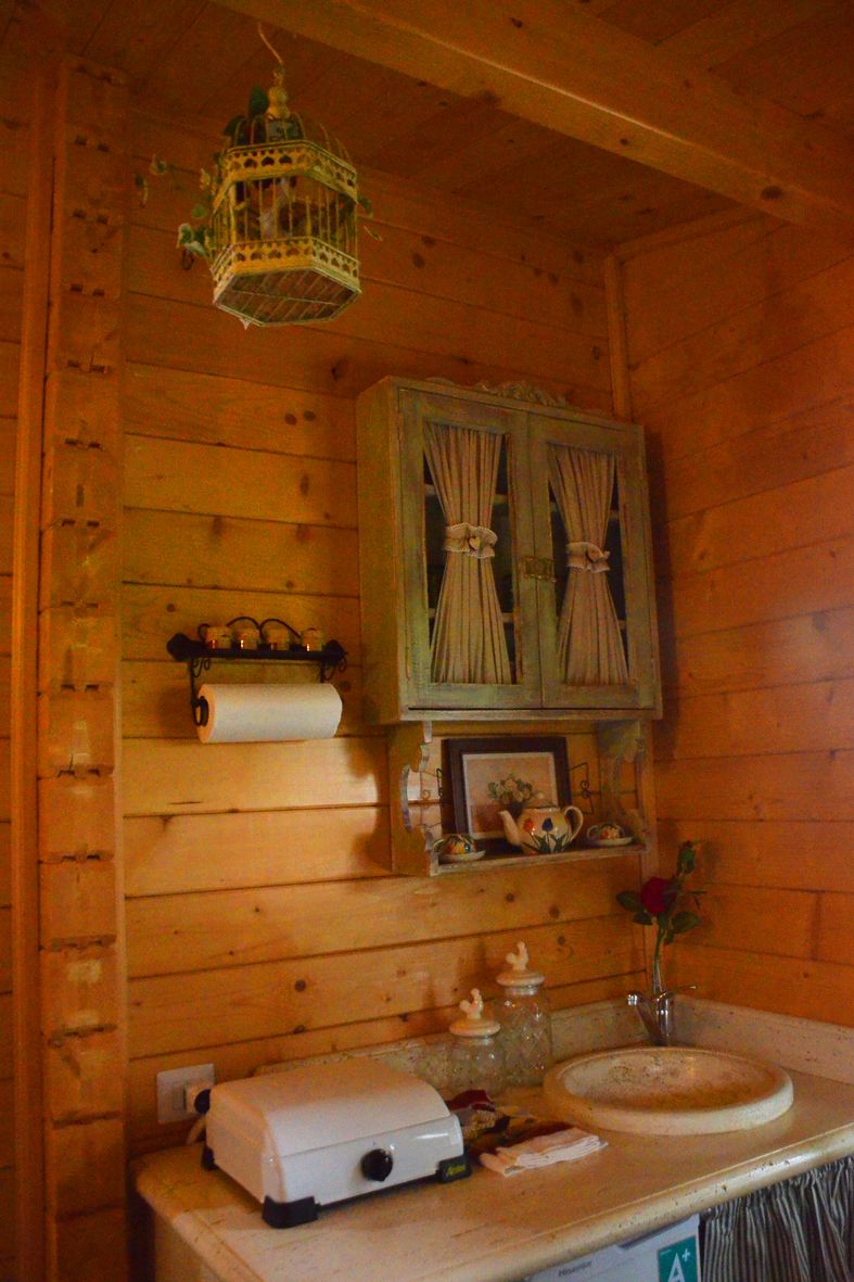 Interno di una baita in legno con un armadietto in legno, un rotolo di carta igienica, un piccolo lavandino e una lanterna decorativa.