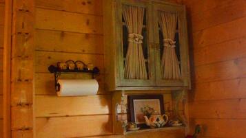 Interno di una baita in legno con un armadietto in legno, un rotolo di carta igienica, un piccolo lavandino e una lanterna decorativa.